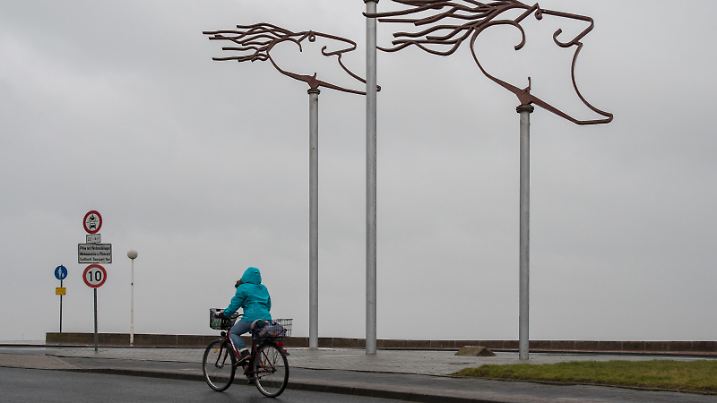 Ein Mädchen kämpft sich am 23.02.2017 mit ihrem Fahrrad gegen den stürmischen Westwind an der Plastik _Windwächter_ in Wilhelmshaven (Niedersachsen) vorbei. An der Nordseeküste wird erst in der Nacht mit dem Eintreffen des Orkantiefs _Thomas_ gerechnet. Foto: Ingo Wagner/dpa | Verwendung weltweit