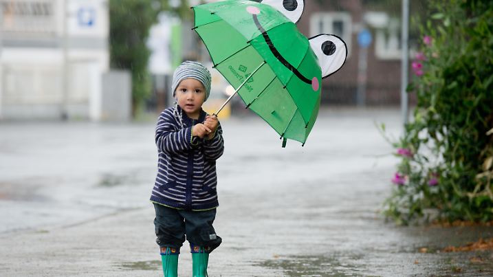 Der einjährige Noah läuft am 19.08.2013 mit einem Regenschirm in Form eines Froschgesichts über eine Straße in Hannover (Niedersachsen). Foto: Julian Stratenschulte/dpa | Verwendung weltweit