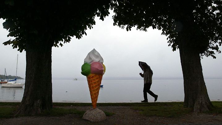 Ein Mann mit Regenschirm läuft am Samstag (01.10.2005) auf der Uferpromenade von Herrsching am Ammersee an einer Reklame-Eistüte vorbei. Ein atlantisches Tiefdruckgebiet bringt Regen und kühle Temperaturen nach Bayern. Noch bis zur Wochenmitte soll laut Wettervorhersage das ungemütliche Schauerwetter andauern. Foto: Karl-Josef Hildenbrand dpa/lby +++(c) dpa - Bildfunk+++