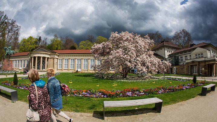 Viele Blumen und ein Magnolienbaum blühen am 12.04.2016 bei Sonnenschein vor dem Kursaal in Stuttgart-Bad Cannstatt (Baden-Württemberg), während zugleich dunkle Wolken darüber hinweg ziehen. Foto: Christoph Schmidt/dpa