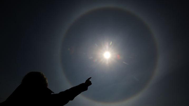 Eine junge Frau zeigt am 29.04.2016 in Purkshof (Mecklenburg-Vorpommern) auf ein Sonnenhalo am Himmel. Ein Halo ist ein Lichtreflex, der durch die Reflexion und Brechung von Licht an Eiskristallen entsteht. Foto: Bernd Wüstneck/dpa | Verwendung weltweit