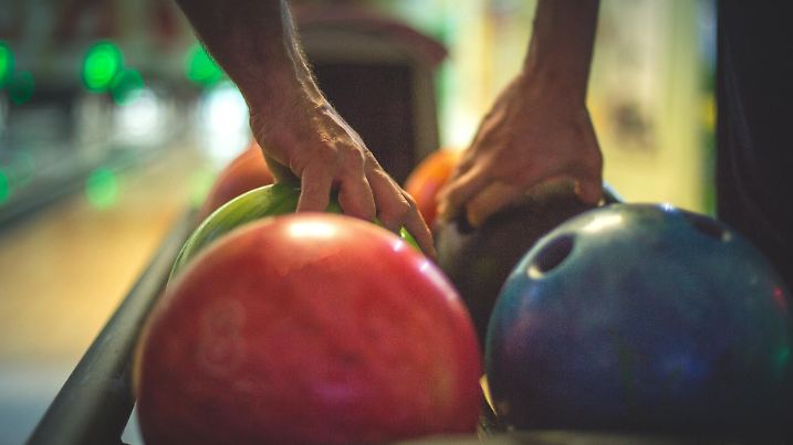 Hände greifen zur Bowlingkugel an der Bowlingbahn