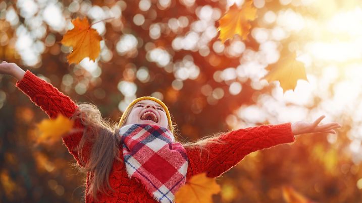 Kind wirft Herbstlaub durch die Luft