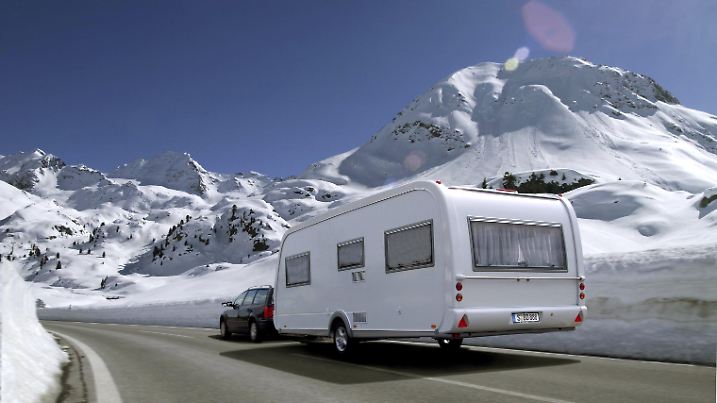 Ein Auto transportiert einen Wohnwagen durch eine verschneite Gebirgslandschaft. Aufnahme vom 11.5.2000. Ein Urlaub mit dem Wohnwagen oder Caravan hat viele Vorteile: Mit dem Wohnwagen hat man sein Bett immer dabei und muss nicht im Hotel übernachten. Und außerdem kann man fast überall, wo es gefällt und zugelassen ist, seinen Wohnwagen parken und einfach Urlaub machen fernab vom Trubel und Pauschaltourismus.