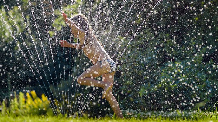 20.06.2018, Saarland, Saarbrücken: Lilo springt im Garten durch das Wasser eines Rasensprengers. Die hochsommerlichen n laden zu der Abkühlung ein. Foto: Oliver Dietze/dpa +++ dpa-Bildfunk +++